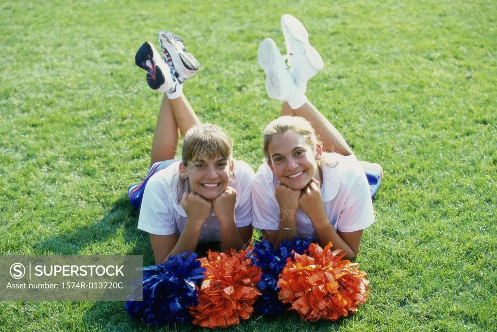 Portrait of two cheerleaders lying down on a field with pom-poms in front of them