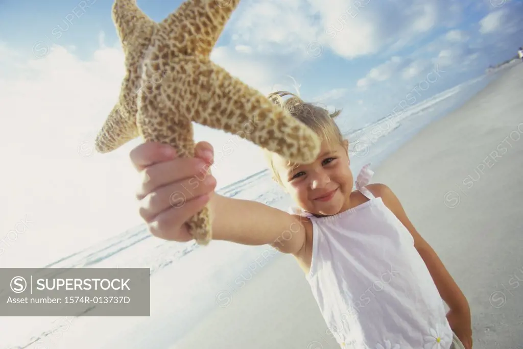 Close-up of a girl showing a starfish on the beach