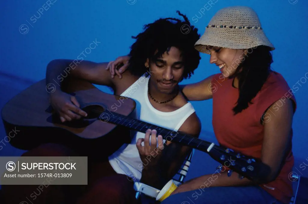 Close-up of a teenage boy playing a guitar with a teenage girl sitting beside him