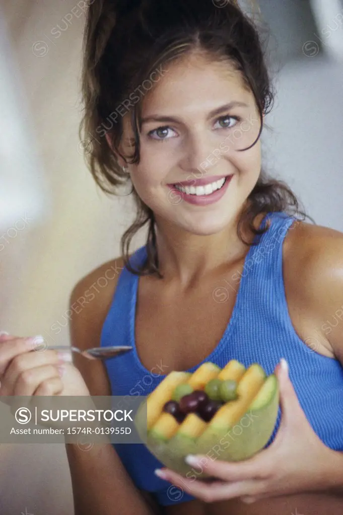 Portrait of a young woman eating a cantaloupe with grapes