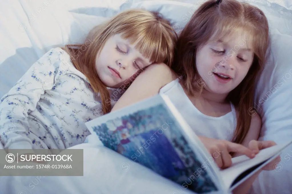 Close-up of two girls reading a book in bed