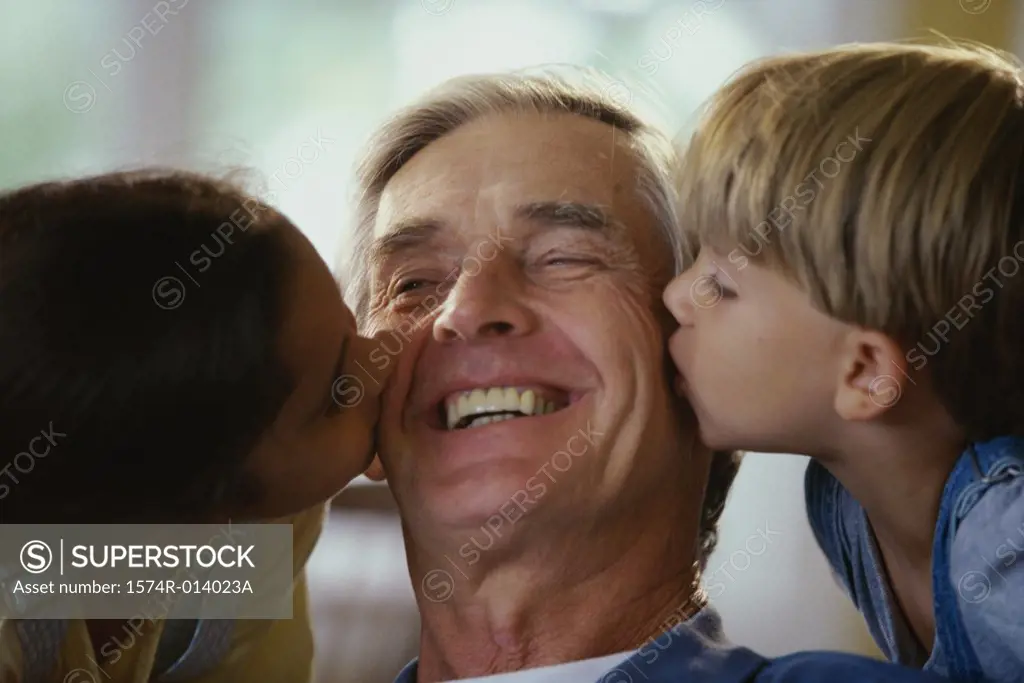 Close-up of a grandson and granddaughter kissing their grandfather