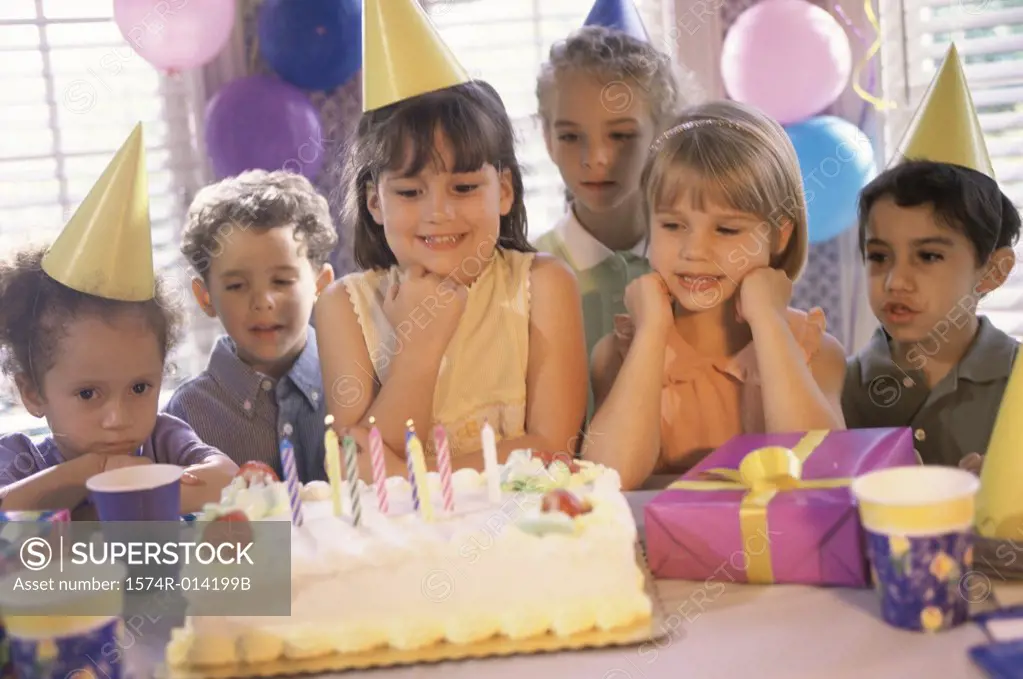 Group of children standing in front of a birthday cake at a birthday party
