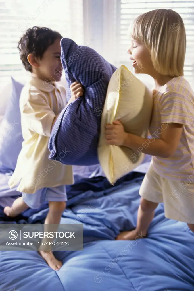 Brother and sister having a pillow fight on the bed