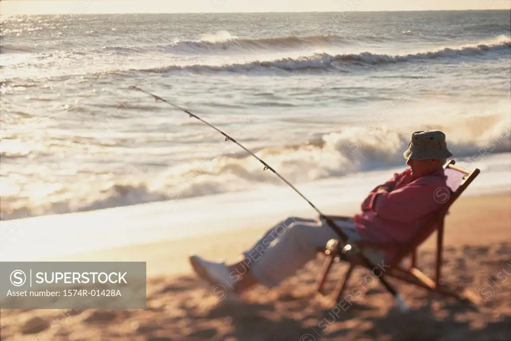 Senior man sitting on a beach chair with a fishing rod