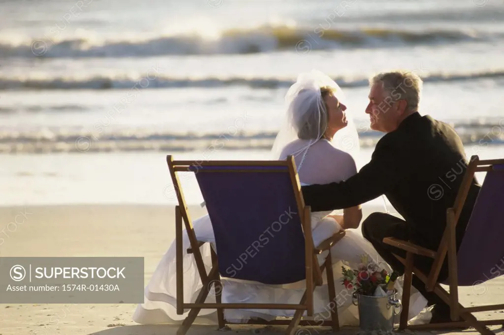 Rear view of a bride and bridegroom sitting on the beach