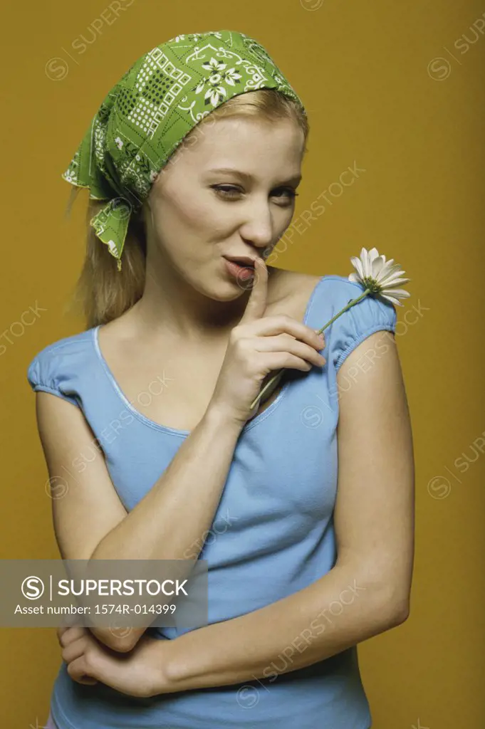 Portrait of a teenage girl holding a flower with a finger on her lips