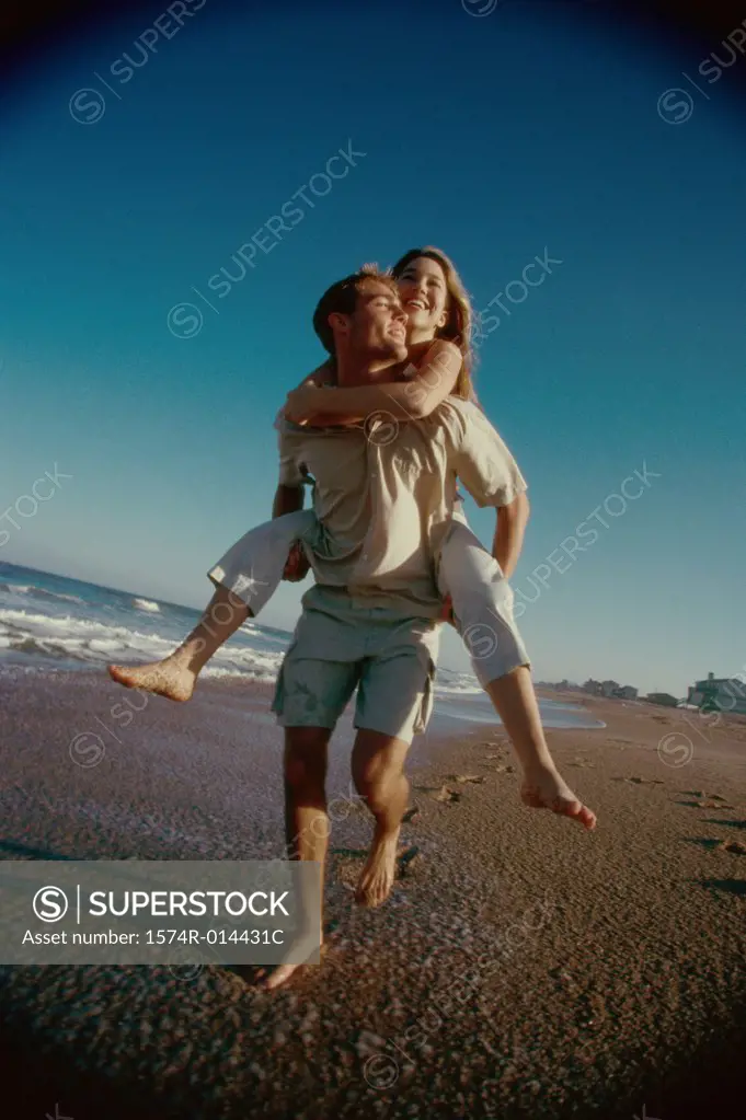 Teenage girl riding piggyback on a young man on the beach