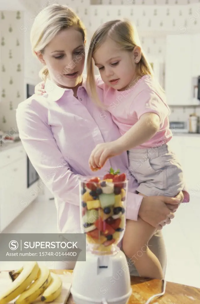 Mother carrying her daughter in front of a blender