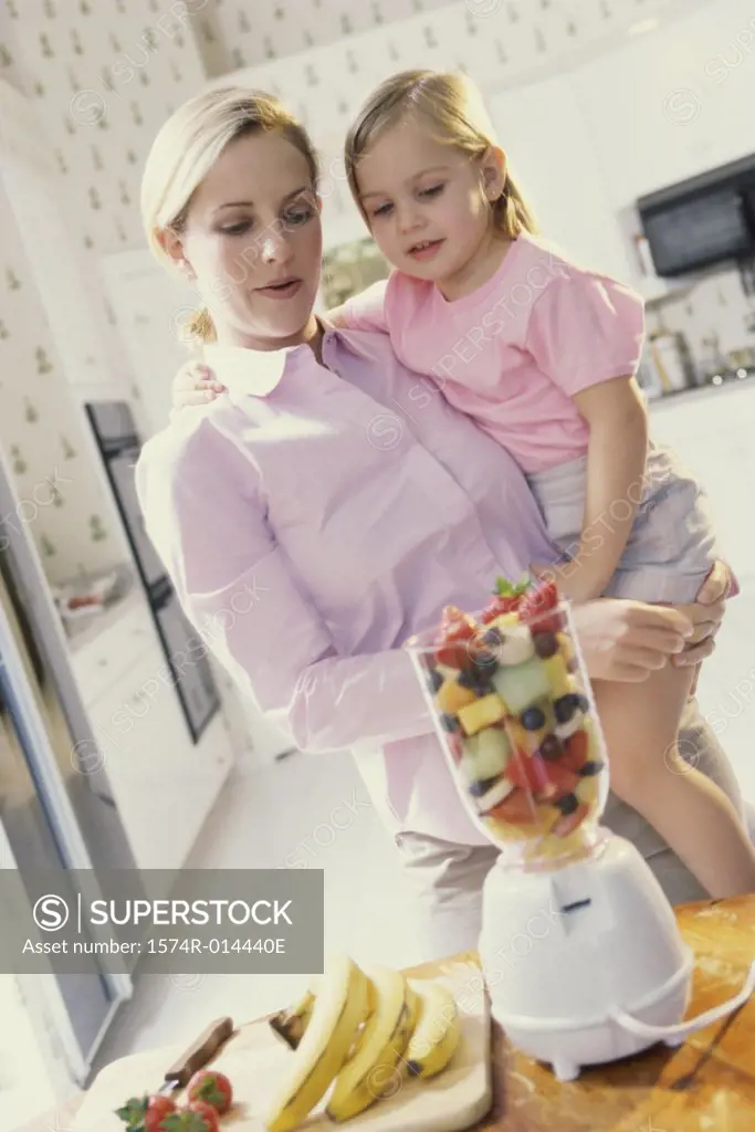 Mother carrying her daughter in front of a blender