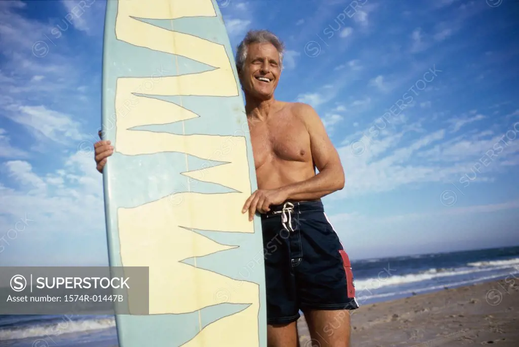 Senior man at the beach holding a surfboard