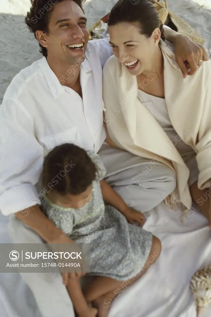 High angle view of parents and their daughter laughing on the beach