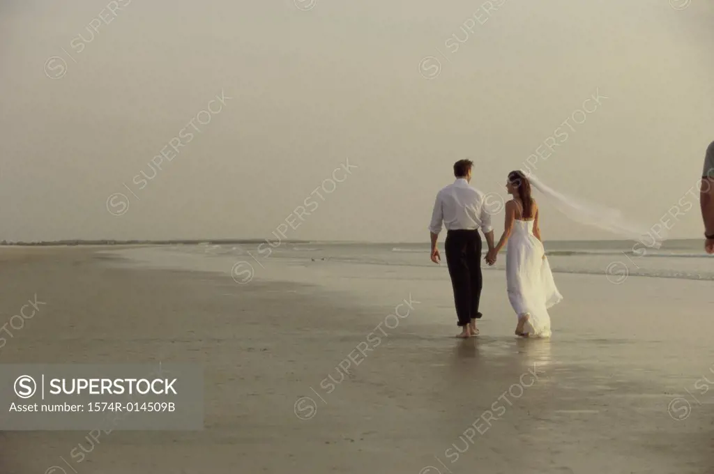 Rear view of a newlywed couple walking on the beach