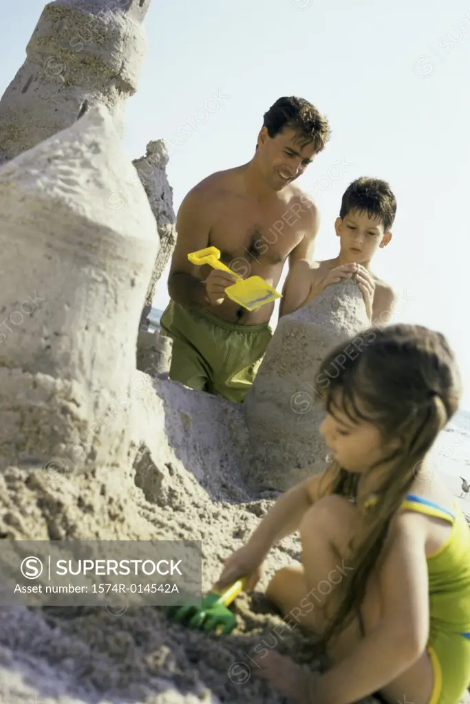 Father making a sand castle on the beach with his son and daughter