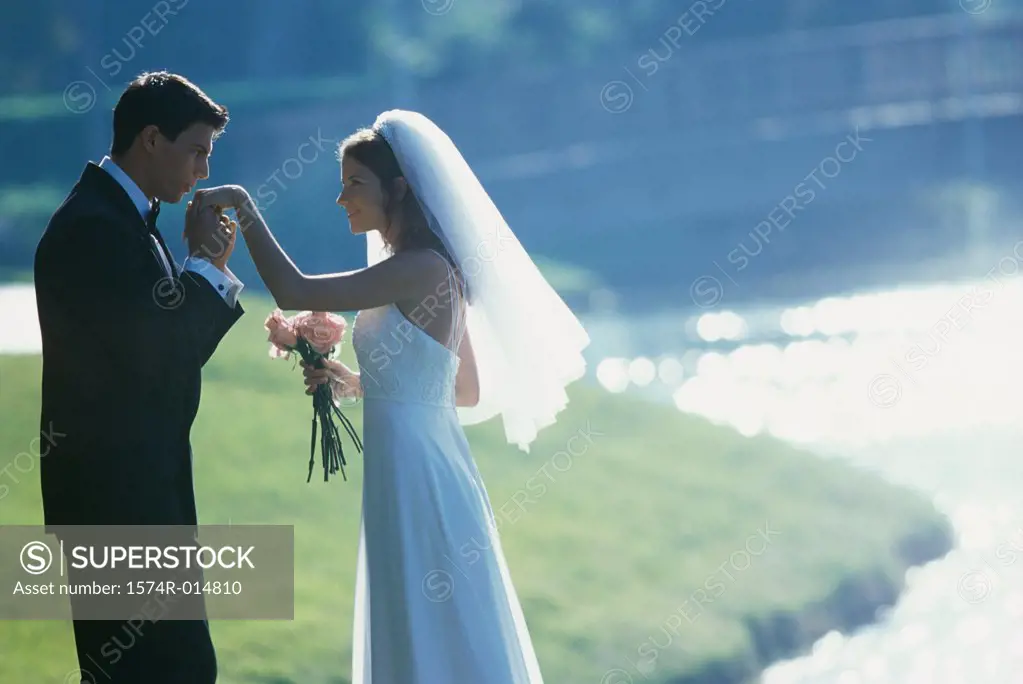 Side profile of a groom kissing his bride's hand near a lake