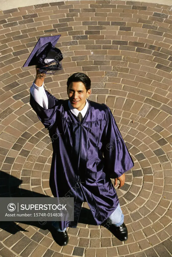 High angle view of a teenage graduate boy raising his mortarboard