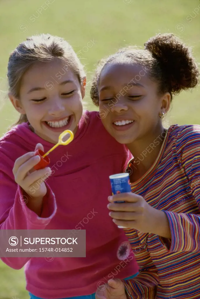 Close-up of two girls holding a bubble wand and smiling