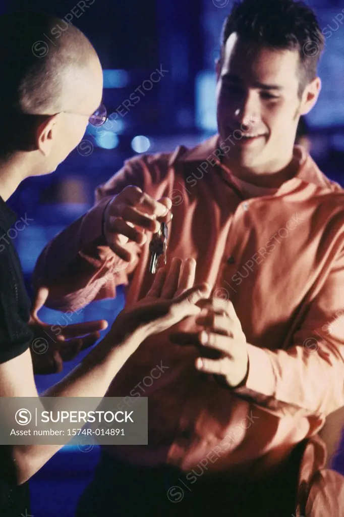 Close-up of a young man giving a car key to his friend
