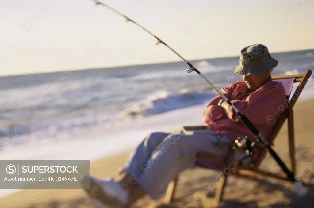Senior man relaxing in a chair with a fishing rod on the beach