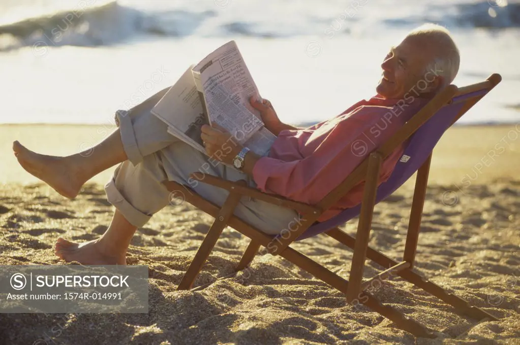Side profile of a senior man reading a newspaper on the beach