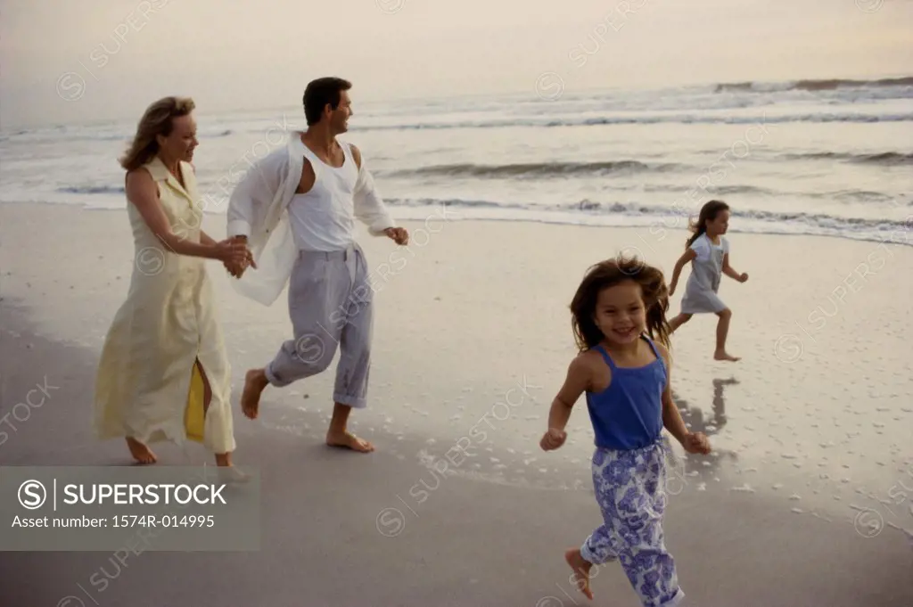 Parents and their two daughters running on the beach