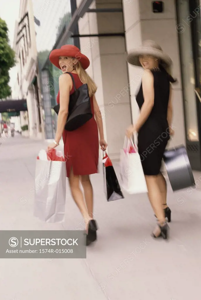 Rear view of two young women carrying shopping bags walking on a sidewalk