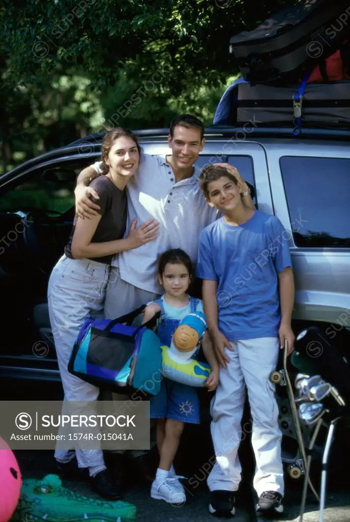 Portrait of parents with their son and daughter standing in front of a car