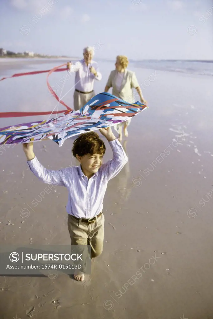 Child flying a kite on the beach with his grandparents