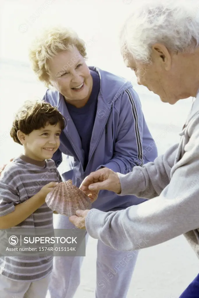 Boy holding a seashell on the beach with his grandparents