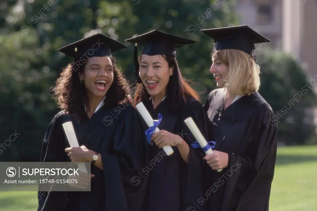 Three young women wearing graduation gowns and holding diplomas