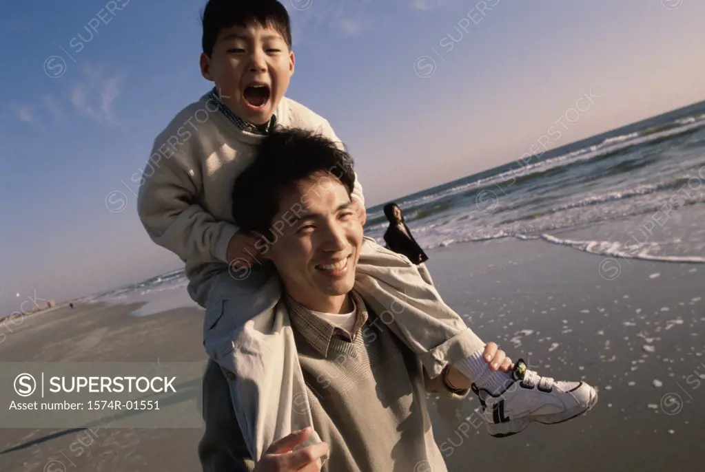 Close-up of a man carrying his son on his shoulders at the beach