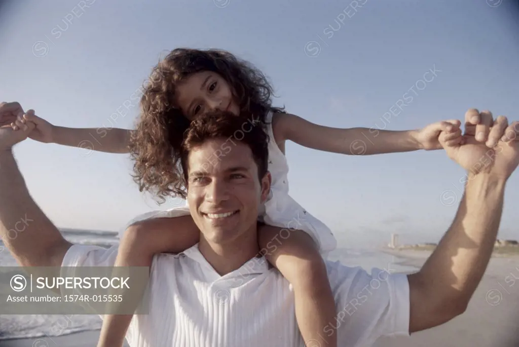 Close-up of a father carrying his daughter on his shoulders at the beach