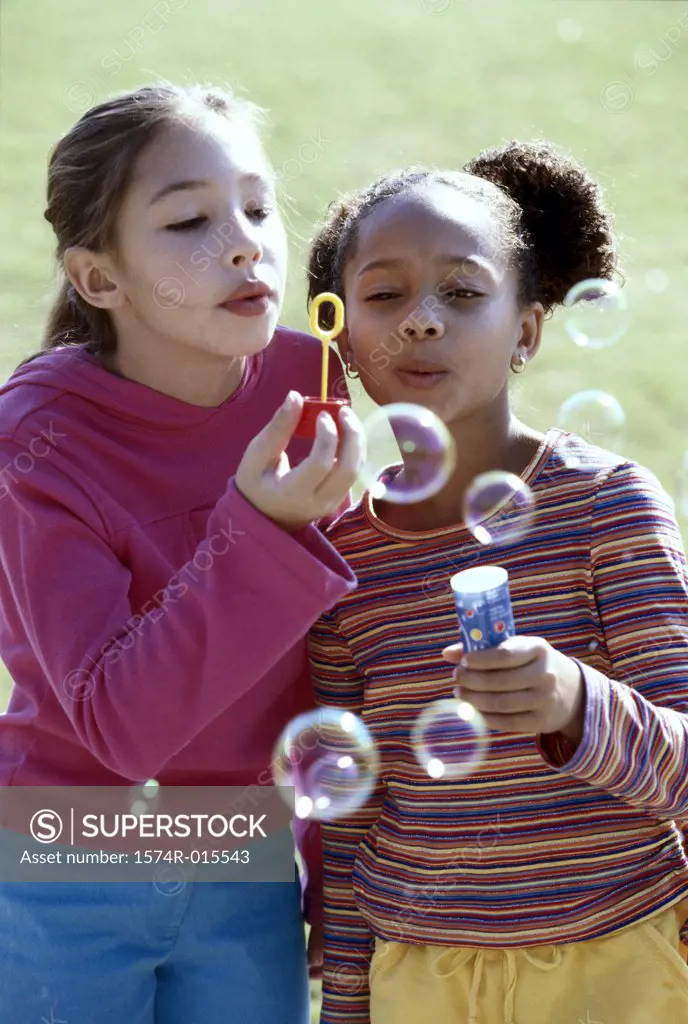 Close-up of two girls blowing bubbles with a bubble wand