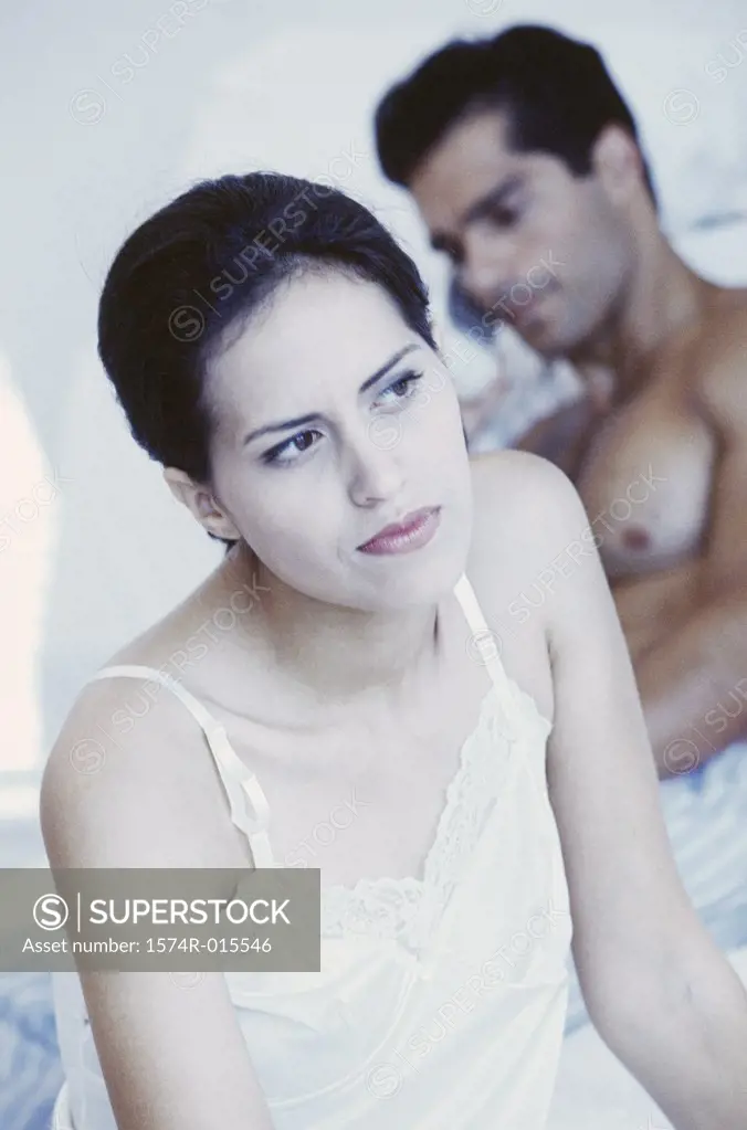 Close-up of a young woman with a young man sitting behind her in bed