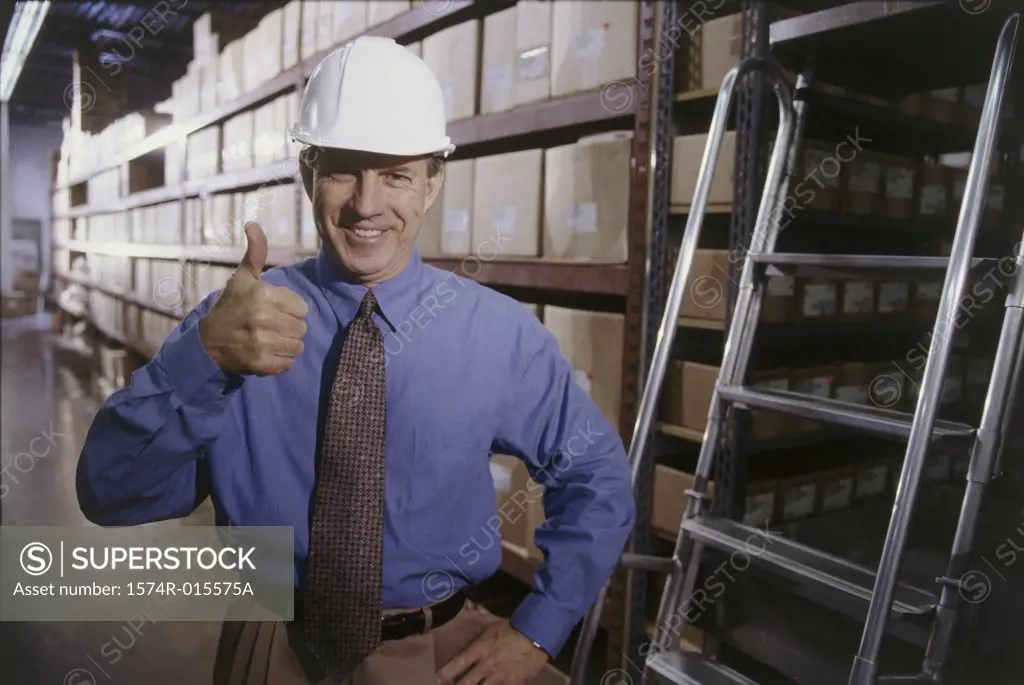 Portrait of a mid adult man making a thumbs up sign in a warehouse