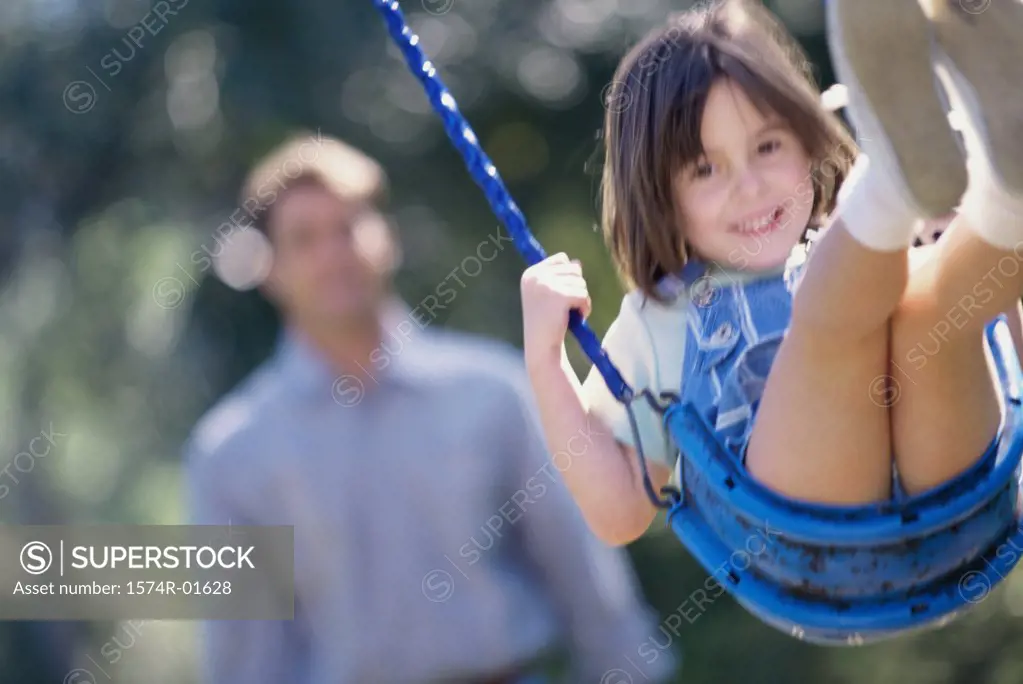 Close-up of a girl on a swing with her father standing behind