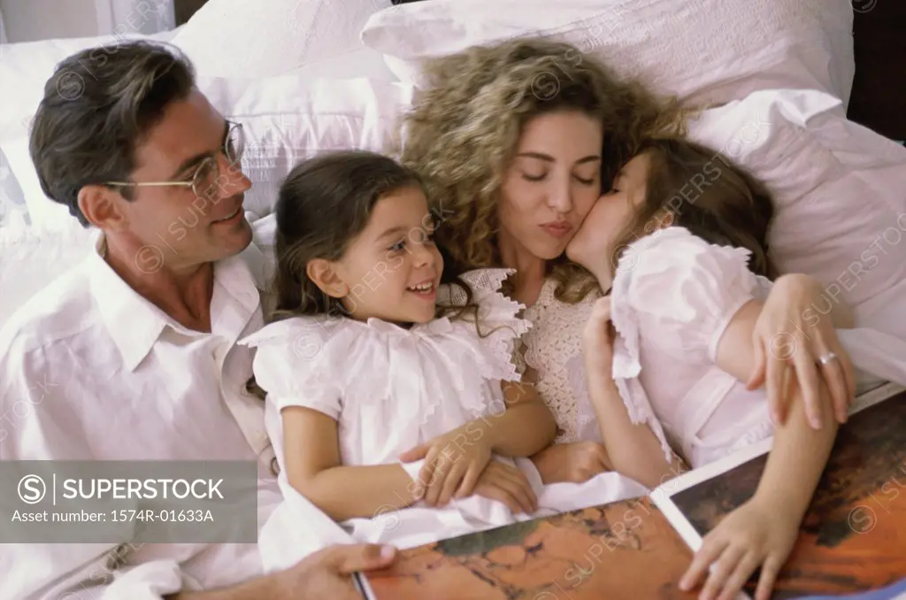 Father and mother lying in bed with their two daughters