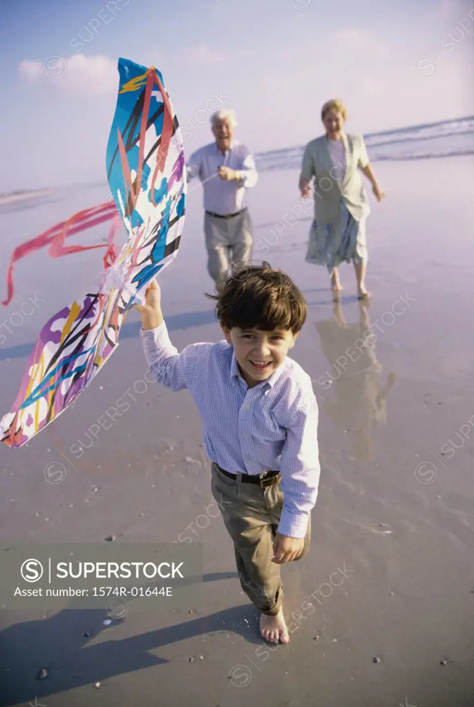 Boy flying a kite on the beach with his grandparents