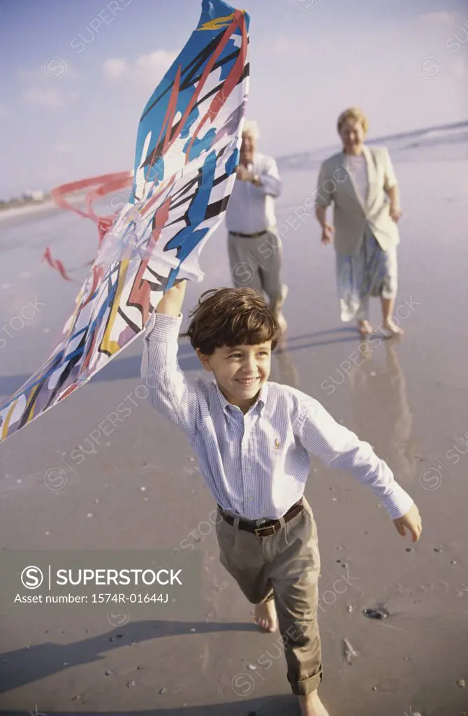 Child flying a kite at the beach with his grandparents