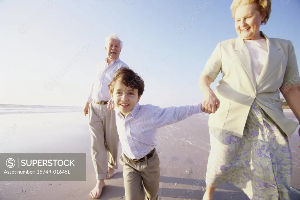 Close-up of a boy holding his grandparents hands on the beach