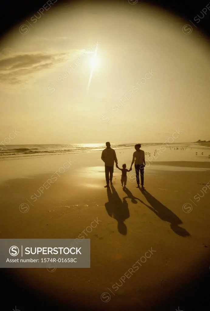 Silhouette of a father and a mother with their daughter at the beach