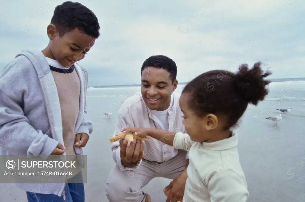 Father showing a starfish to his son and daughter on the beach