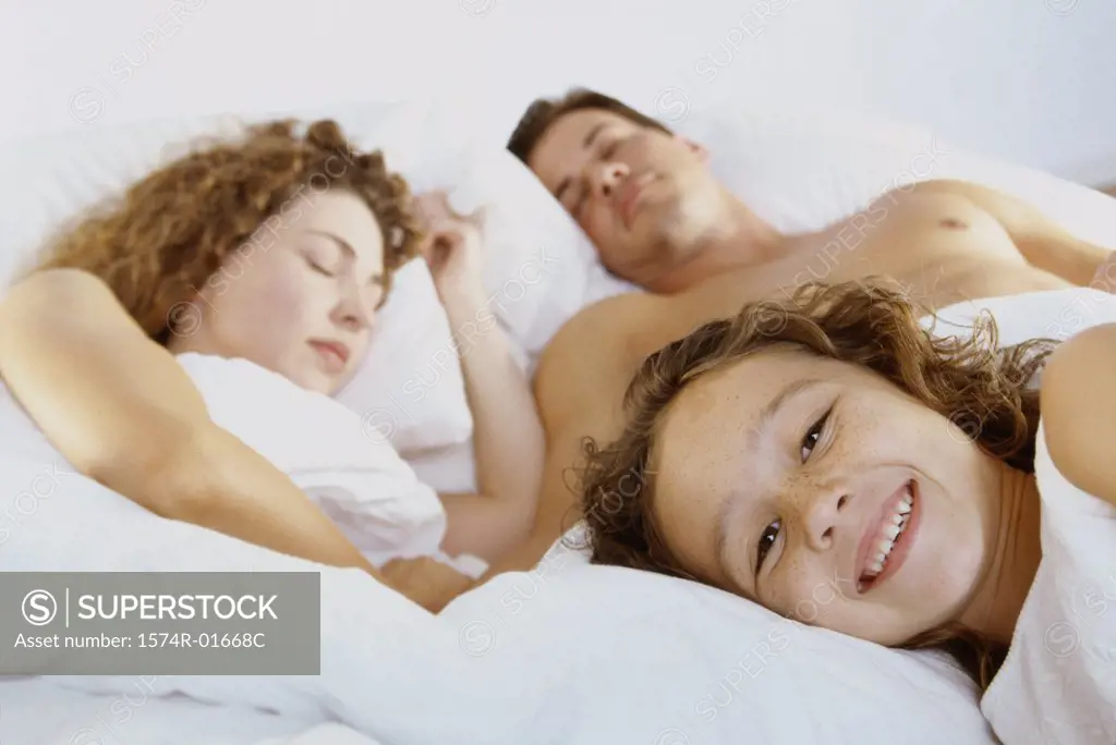 Close-up of a girl lying with her parents in bed