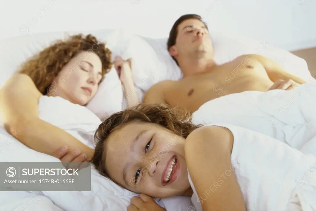 Portrait of a girl smiling with her parents sleeping on a bed behind her