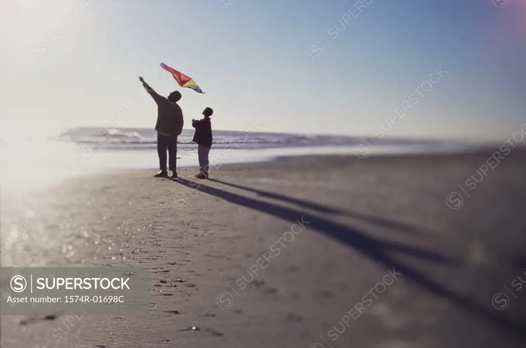 Silhouette of a father and son flying a kite on the beach