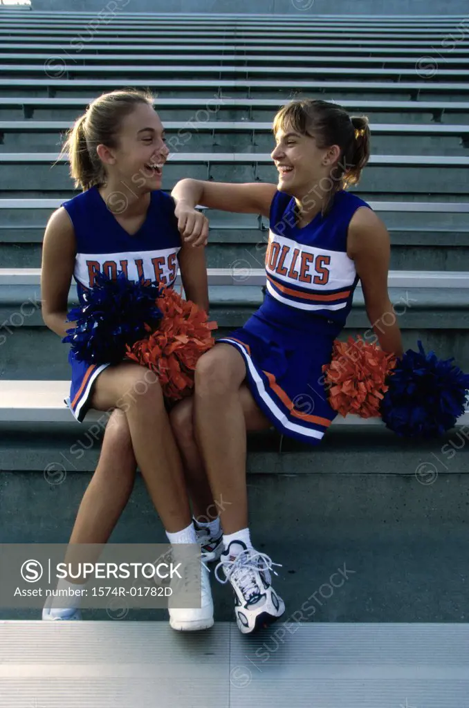 Two cheerleaders sitting with pom-poms