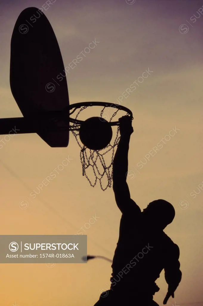 Silhouette of a man slam dunking a basketball
