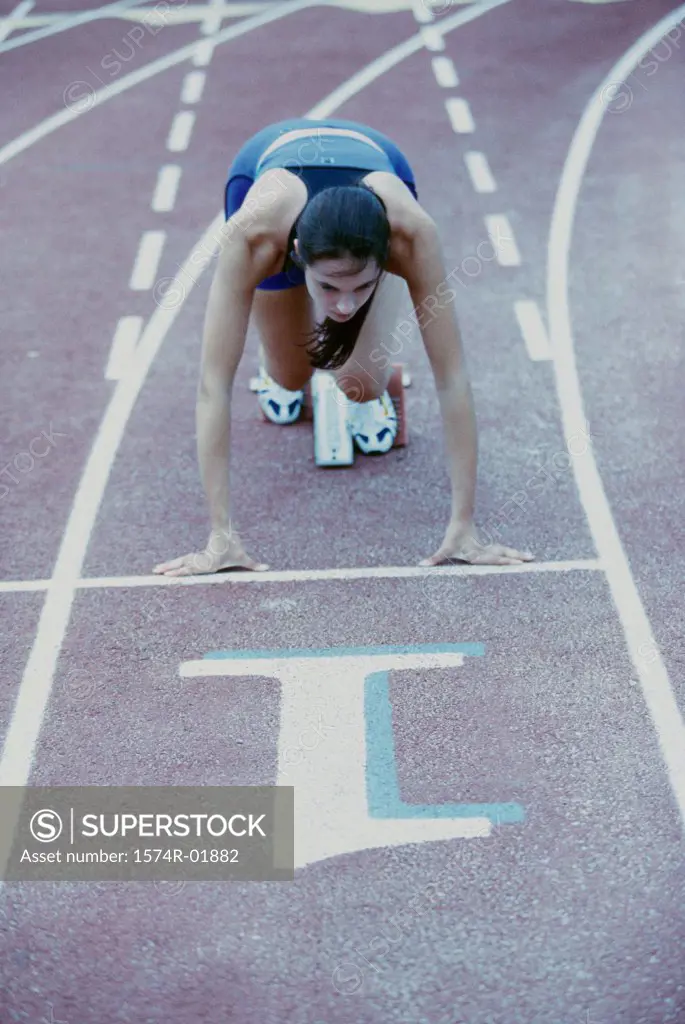 High angle view of a young woman at the starting position of a running track