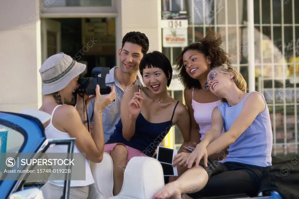 Teenage girl taking a photograph of a teenage boy and three teenage girls in a car