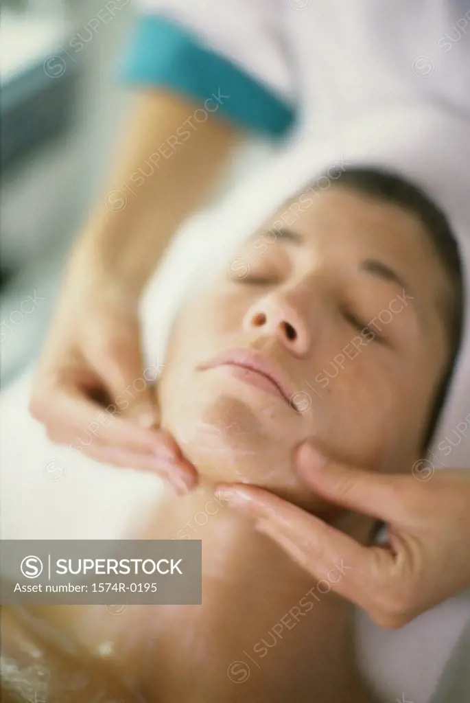 Close-up of a person's hands massaging a young woman's face